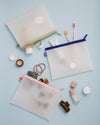 The Letterfolk 3 Piece Pouch Set with hair accessories and cosmetics on a blue background.