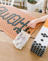 An image of a person using the Letterfolk Black tiles to design their Letterfolk Clay Tile Mat on a wooden table.