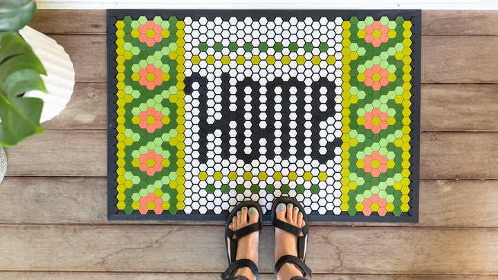 A overhead shot on the Letterfolk Tile Mat with feet on it on a wooden surface. 