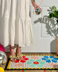 A woman wearing gold heels standing on the Letterfolk Tile & Mat Set Advance Bundle designed on a Tile Mat in front of a doorway. 