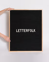 2 Hands holding up the Letterfolk Oak Wordsmith Letter Board against a grey background. 