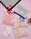 The Letterfolk 3 Piece pouch Set with a Tile Mat and Tile Set on a pink background. 