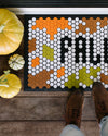 A close up of the Letterfolk Harvest Tile Set on a Tile Mat Design displayed with shoes and pumpkins on a wooden floor. 