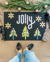 The Letterfolk "Jolly" Black Tile Mat used as part of a festive display on a wooden floor.