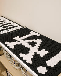 The Letterfolk Black Tile Mat on a white shelf. 