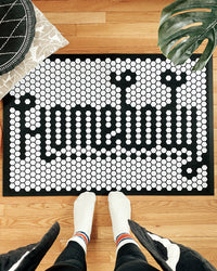 An image of a person standing over the Letterfolk White Tile Mat "Homebody" design on a wooden floor. 