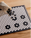 A close up image of the Letterfolk White Tile Mat with black tiles spilled out from a mesh storage bag onto the mat, placed on a wooden floor.