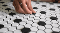 A hand placing Letterfolk Black Tiles on a Letterfolk White Tile Mat. 